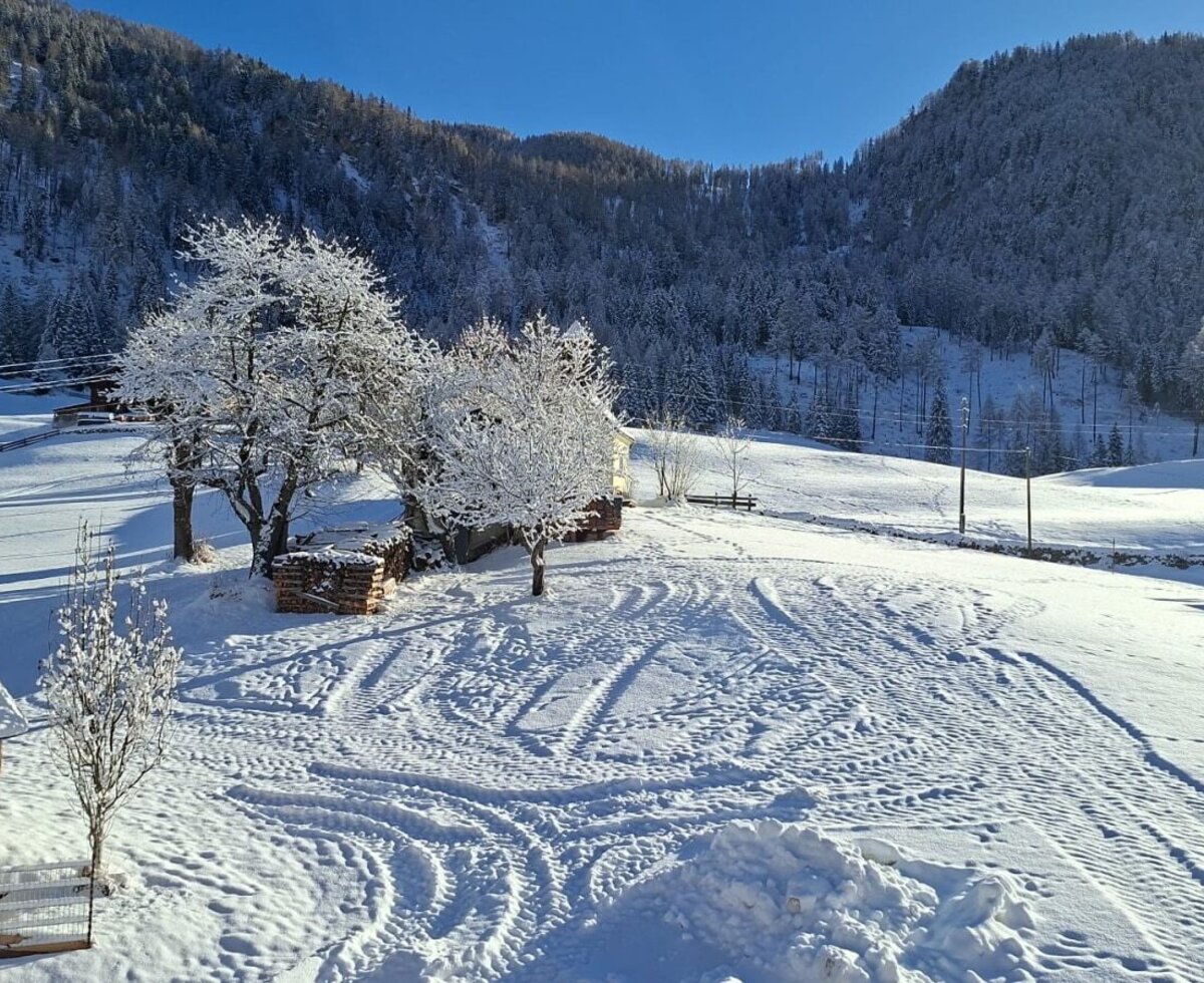 Sonnige Winterlandschaft des Bauernhofs mit verschneiten Feldern und bewaldeten Bergen.