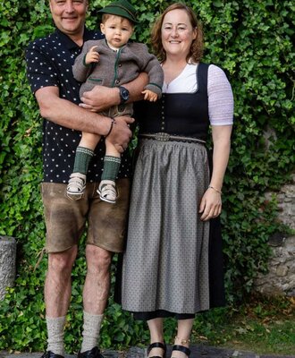 Die Gastgeberfamilie des Bauernhofs in traditioneller Tracht vor einer mit Efeu bewachsenen Wand.