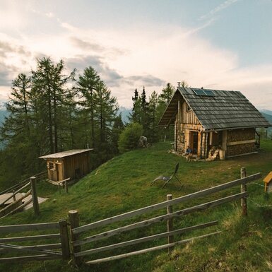 Die Almhütte mit dem separaten Panorama Badehäuschen und dem Hot Tub, gelegen auf einer Wiese mit Bergblick.