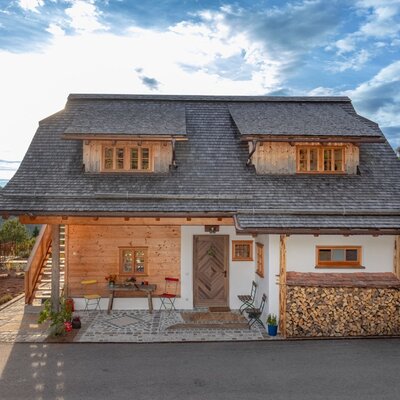 Außenansicht des Ferienhauses mit Holzfassade, weiß verputzten Wänden, Schindeldach, einer Terrasse mit Sitzgelegenheiten und einem Holzstapel.