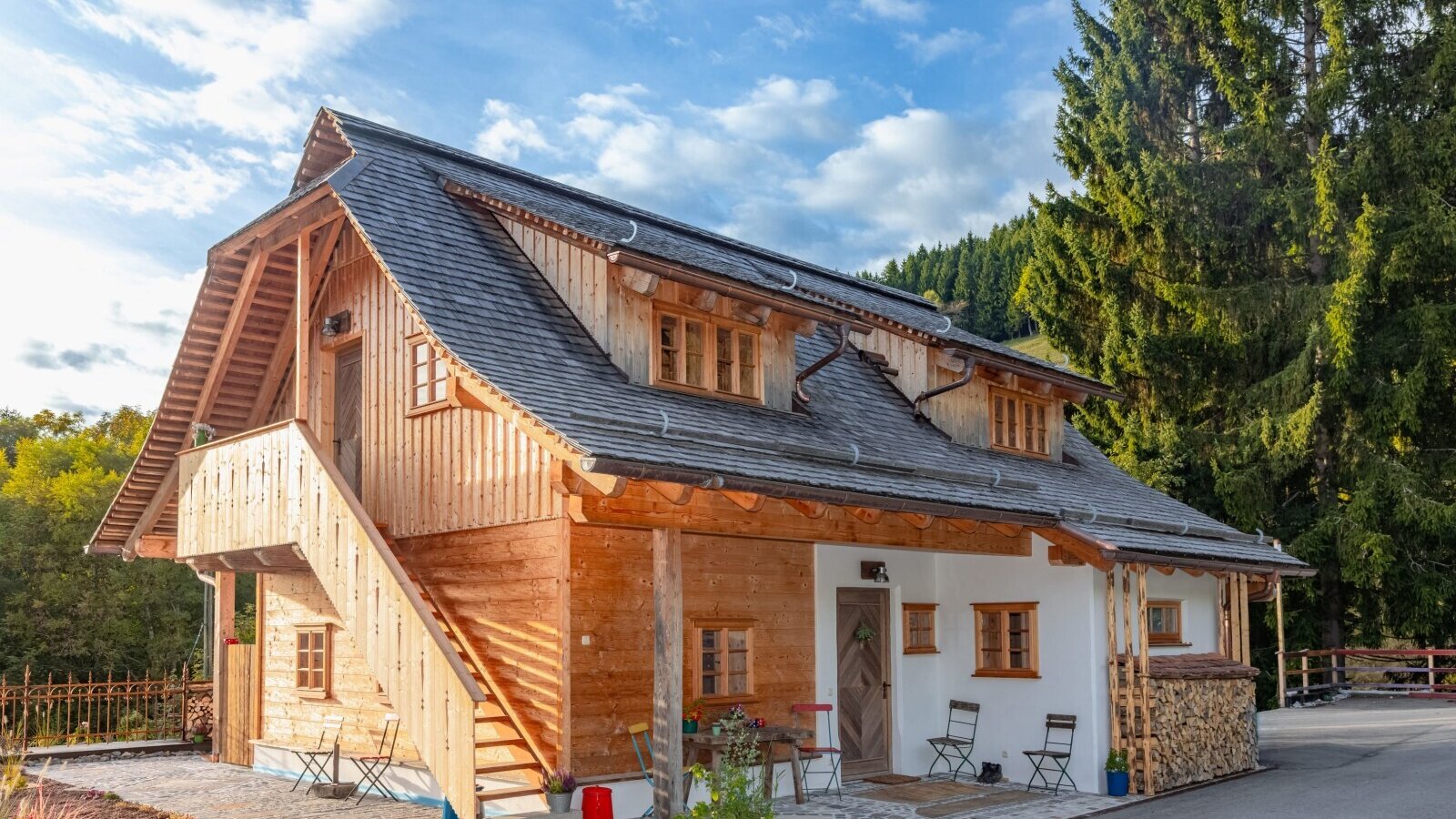 Das Ferienhaus mit Holzfassade, weiß verputzten Wänden, einer Außentreppe und einer Terrasse mit Sitzgelegenheiten.