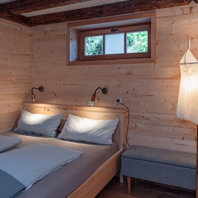 Schlafzimmer im Ferienhaus mit Doppelbett, Holzwänden, Leselampen und einem Fenster.