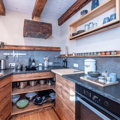 Voll ausgestattete Küche im Ferienhaus mit Induktionskochfeld, Backofen, Geschirr und rustikalen Holzelementen.
