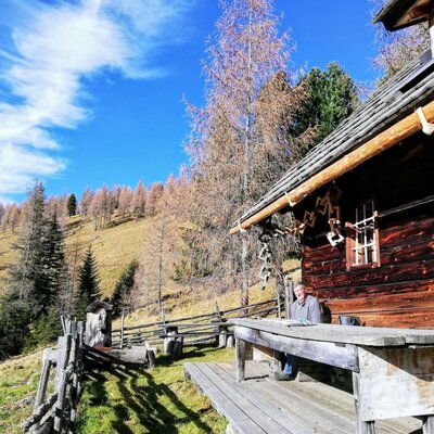 Die Almhütte mit einem Lärchentisch und einer Bank auf der Terrasse, mit Blick auf die Nockberge.
