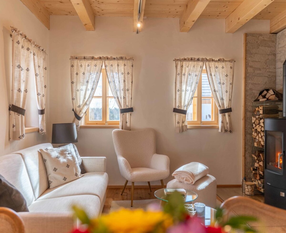 Die Stube des Bauernhofs mit Sofa, Sessel, Kaminofen und Holzbalkendecke.