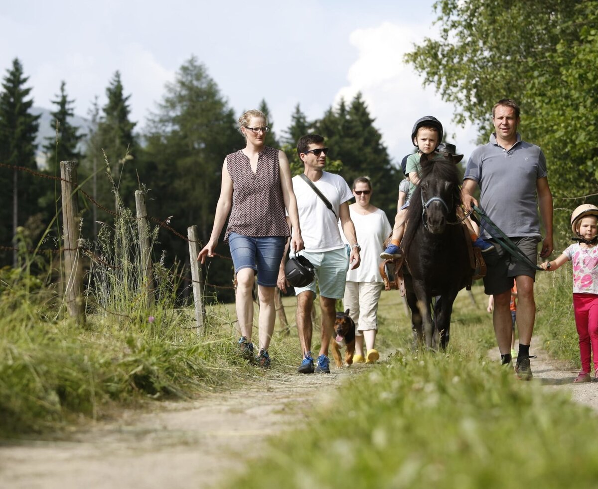 Eine Familie unternimmt einen Ausflug mit Ponyreiten auf einem Feldweg am Bauernhof.