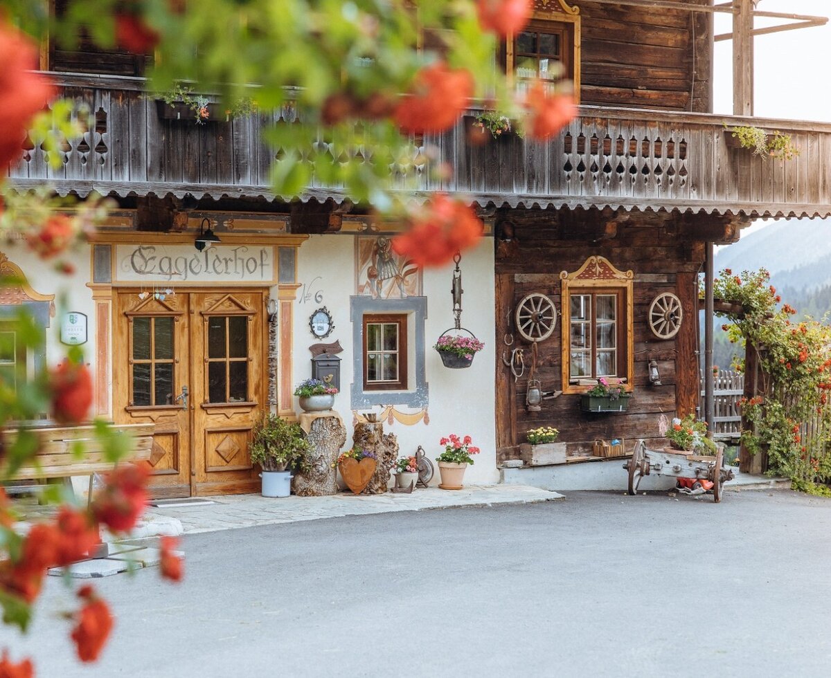 Außenansicht des Bauernhofs "Eggelerhof" mit Holzbalkon, traditionellen Holztüren und bemalter Fassade.