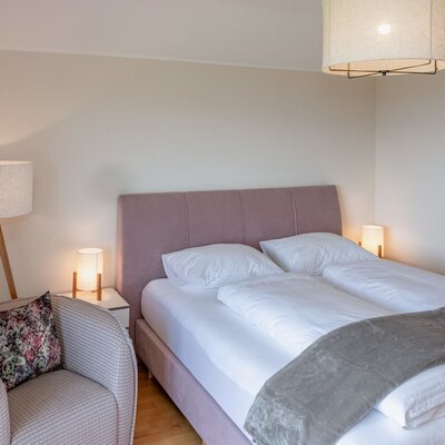 Schlafzimmer im Bauernhof mit Doppelbett, Nachttischen, Leselampen und einem Sessel.