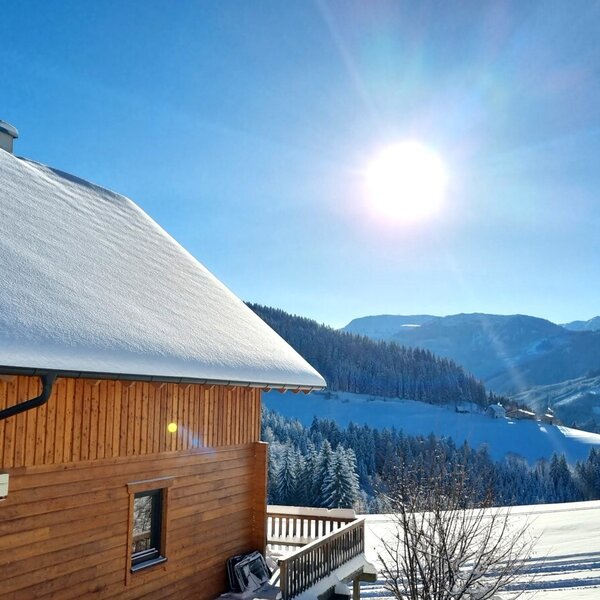Blick vom Ferienhaus auf die verschneite Berglandschaft unter klarem, sonnigem Himmel.