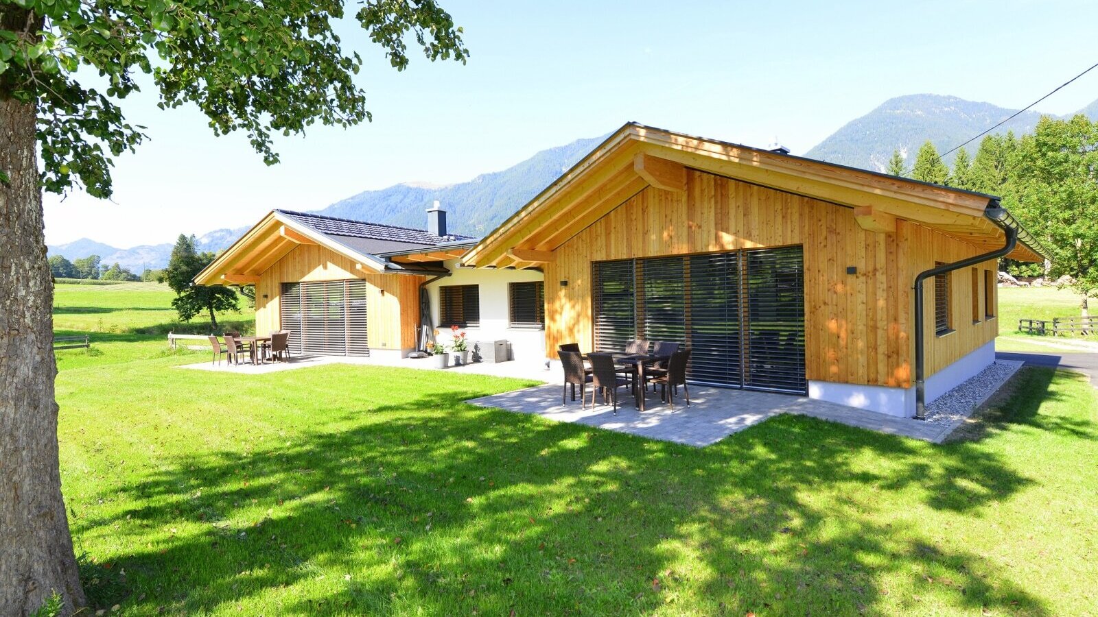 Außenansicht des Bauernhofs mit zwei Gebäuden, möblierten Terrassen und umliegendem Garten mit Bergblick.