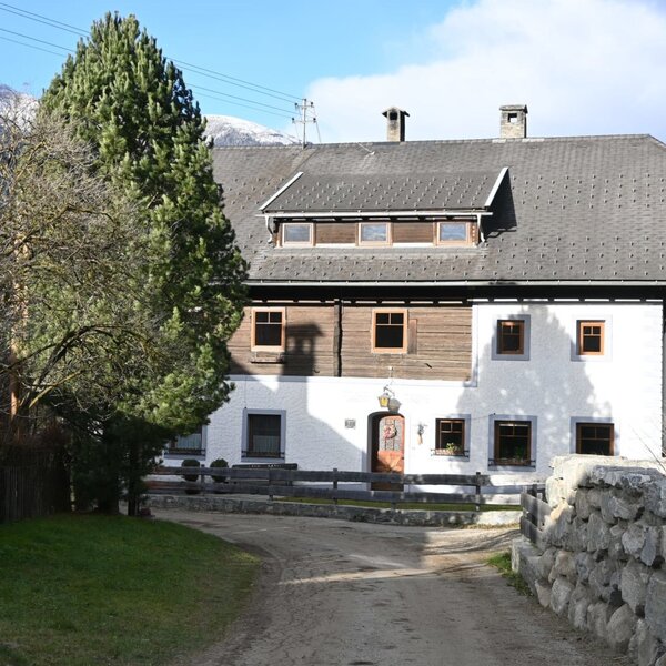 Außenansicht der Ferienwohnung mit weiß getünchten Wänden, Holzverkleidung und einem Zufahrtsweg.