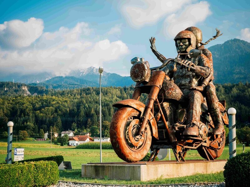Eine eindrucksvolle Motorradskulptur aus Metall auf dem Gelände des Bauernhofs vor einer malerischen Bergkulisse.