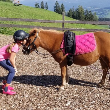 Ein Kind mit Reithelm küsst ein gesatteltes Pony auf dem Bauernhof.