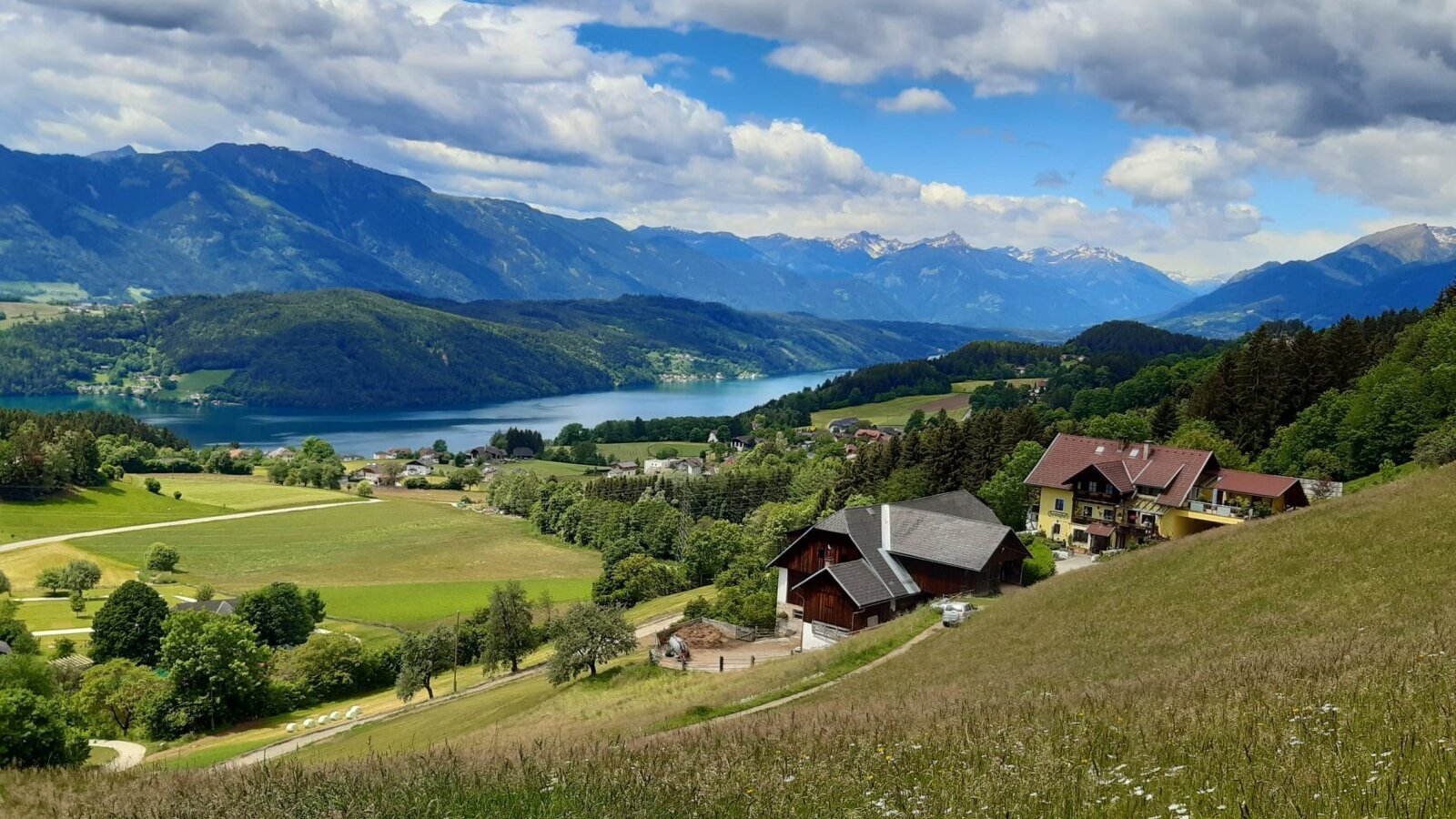 Der einladende Bauernhof, eingebettet in grüne Wiesen mit einem herrlichen Ausblick auf den schimmernden Millstätter See und die umliegende Berglandschaft.