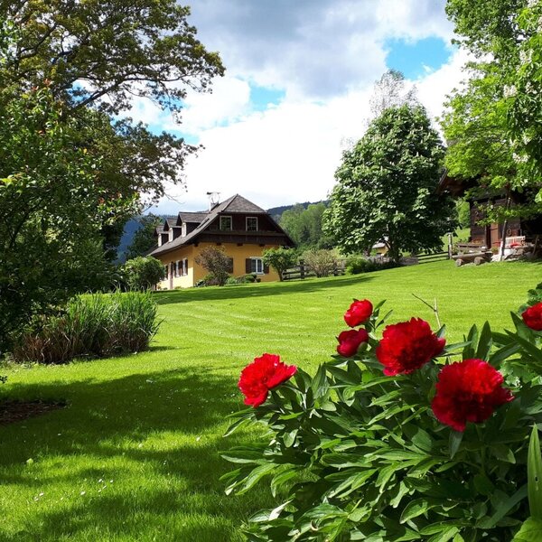 Der Bauernhof mit einem weitläufigen Garten, grünem Rasen und blühenden Pflanzen vor dem Hauptgebäude.
