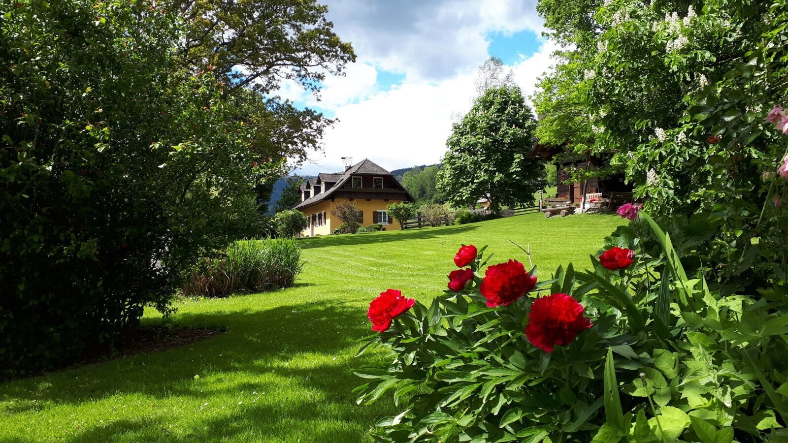 Der Bauernhof mit einem weitläufigen Garten, grünem Rasen und blühenden Pflanzen vor dem Hauptgebäude.