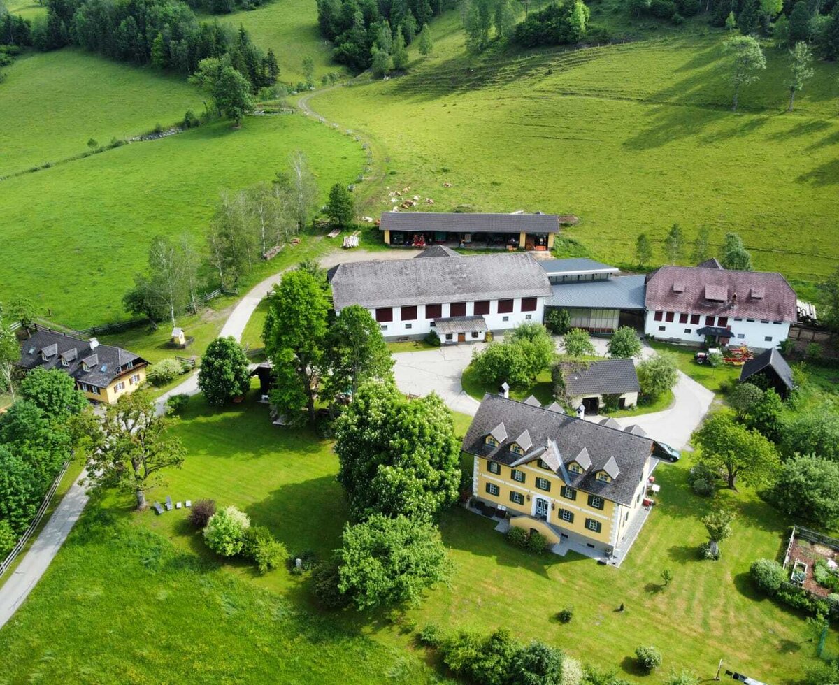 Luftaufnahme des Bauernhofs mit seinen Gebäuden und umliegenden Grünflächen.