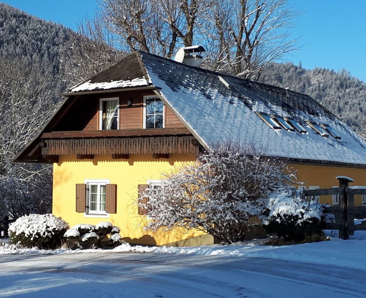 Der Bauernhof mit gelber Fassade und schneebedecktem Dach in winterlicher Berglandschaft.