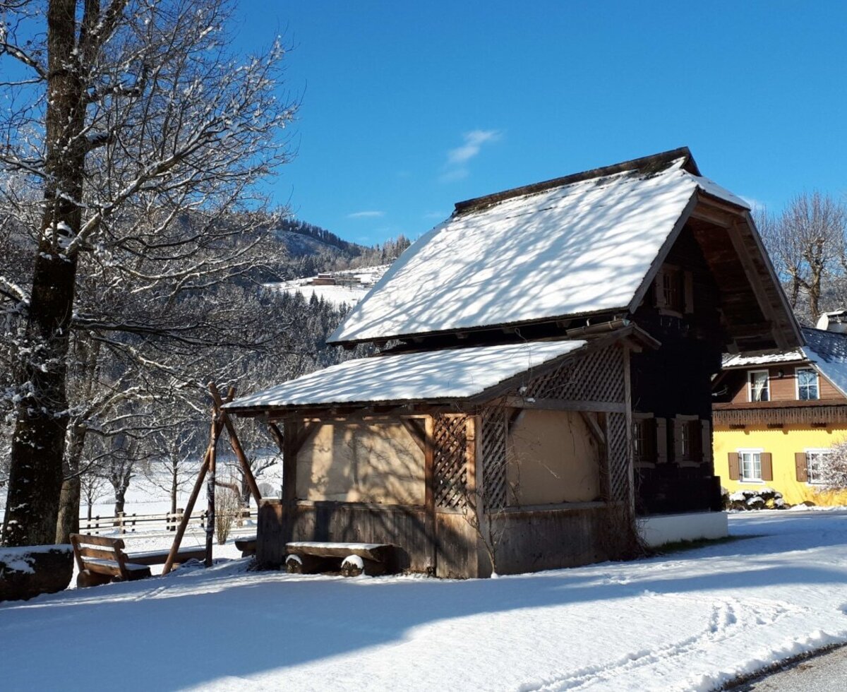 Der Bauernhof im Winter, mit schneebedeckten Gebäuden, Außenbereichen und der umliegenden Winterlandschaft.