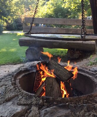 Lagerfeuerstelle auf dem Bauernhof mit brennendem Holzfeuer, einer Schaukelbank und einer Grillplatte.