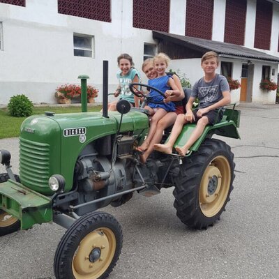Vier Kinder sitzen auf einem Traktor und erleben das Landleben auf dem Bauernhof.