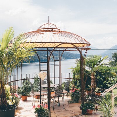 Der Pavillon auf dem Bauernhof mit Tisch und Stühlen und Aussicht auf den See und die Berge.