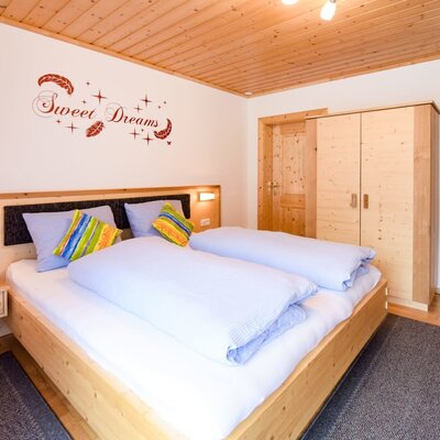 Ein helles Schlafzimmer in der Ferienwohnung auf dem Bauernhof mit gemütlichem Doppelbett und hellen Holzmöbeln.
