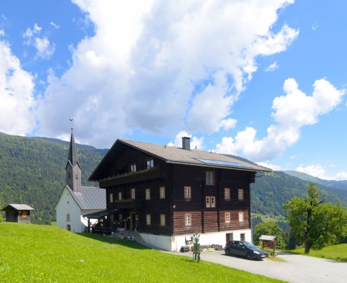 Der einladende Bauernhof inmitten von grünen Wiesen mit Blick auf eine idyllische Kirche und die Lesachtaler Bergwelt.