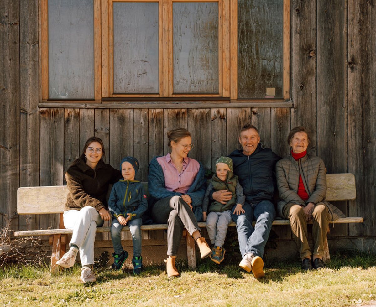Familie Zojer auf einer Holzbank vor der Holzhütte.
