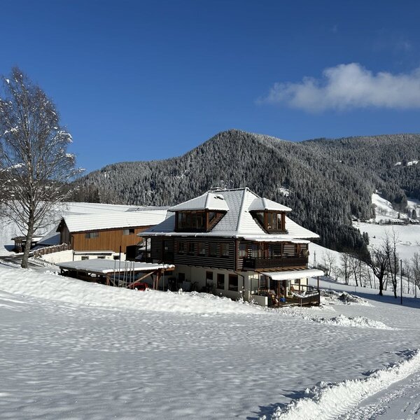 Der Bauernhof in winterlicher Umgebung mit schneebedeckten Feldern und Bergen.