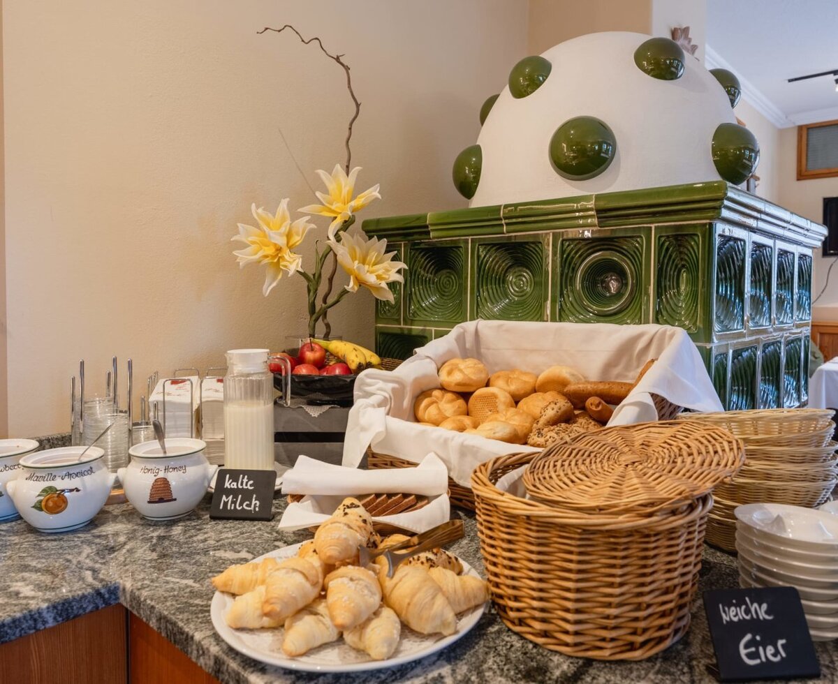Das Frühstücksbuffet im Bauernhof bietet frische Brötchen, Croissants, Marmelade, Honig, Milch und Obst neben einem traditionellen Kachelofen.