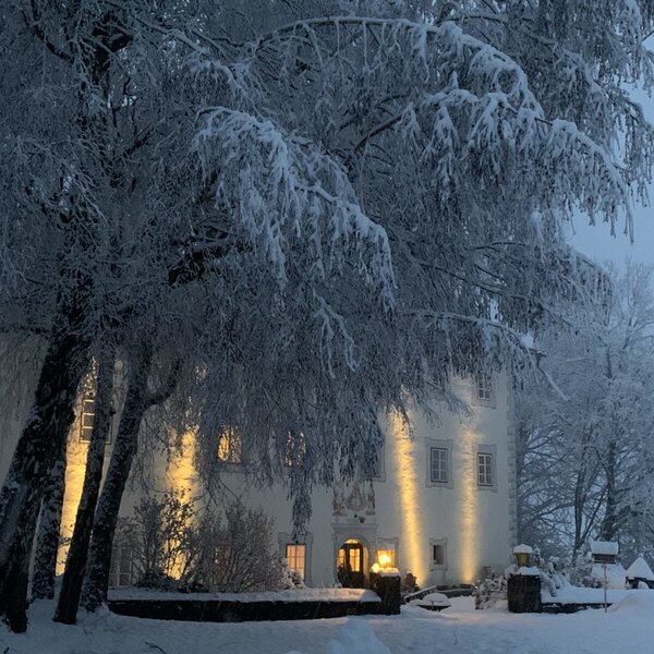 Das stimmungsvoll beleuchtete, historische Gebäude der Ferienwohnung inmitten einer verschneiten Winterlandschaft.