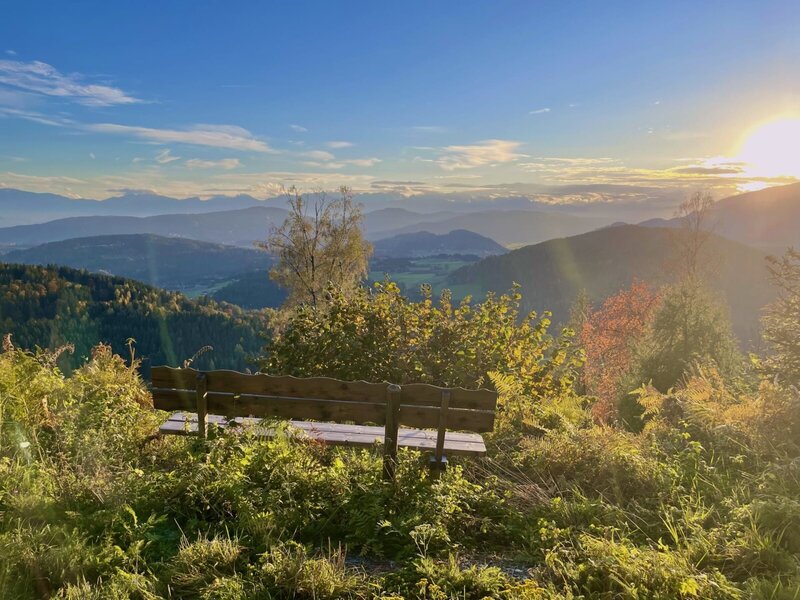 Einladende Holzbank mit malerischem Panoramablick auf die umliegende Bergwelt im warmen Sonnenlicht.