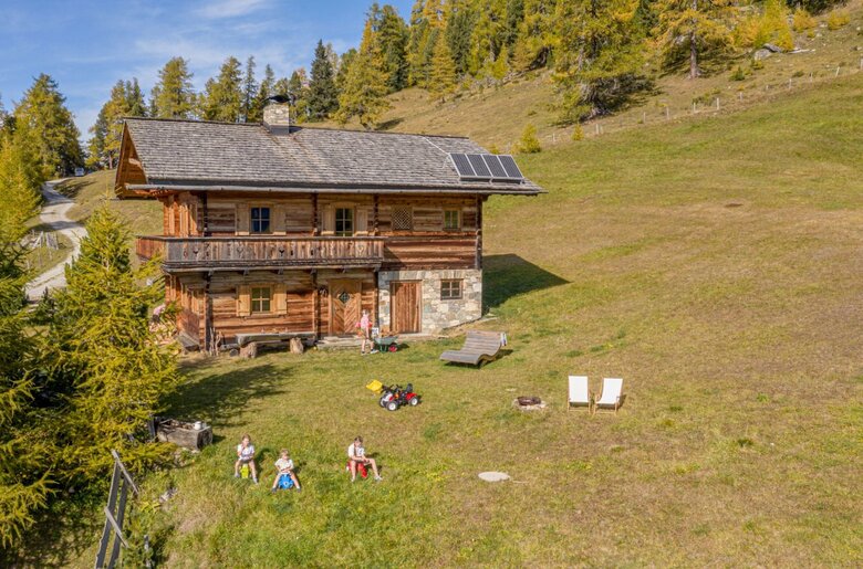 Die Alm mit Holzfassade, Solarpaneelen auf dem Dach, Balkon und einer großen Wiese mit Sitzgelegenheiten.