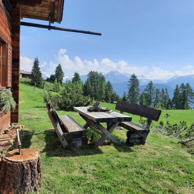 Der Außenbereich der Alm bietet einen Holztisch mit Bänken und Blick auf die Berge.