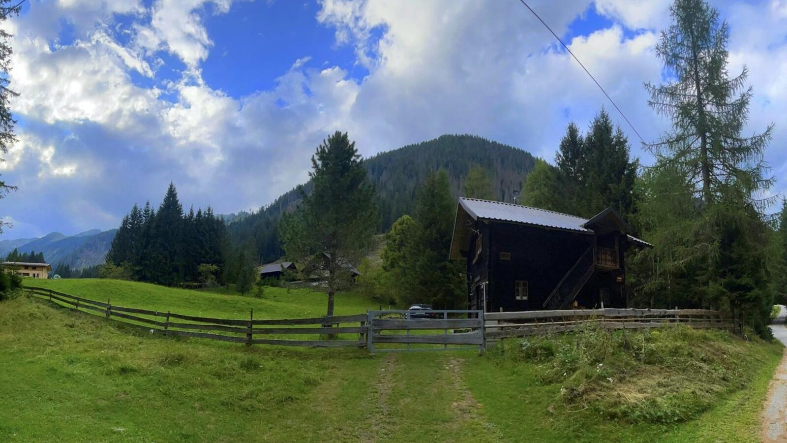 Eine urige Alm inmitten grüner Wiesen, umgeben von dichten Nadelbäumen und sanften Berghängen.