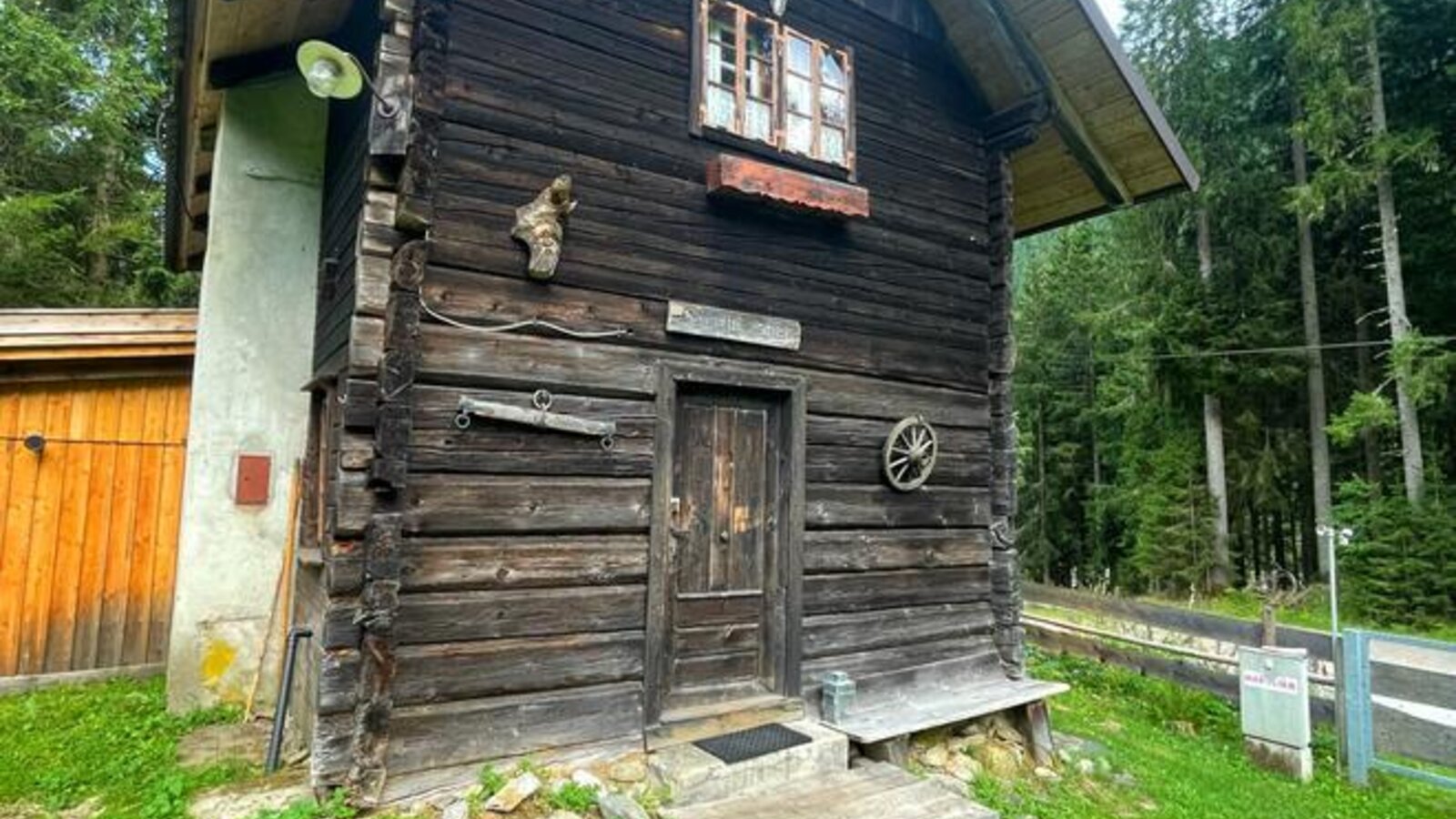 Eine urige Alm mit traditioneller Holzfassade, umgeben von einer grünen Wiese und dichten Wäldern.