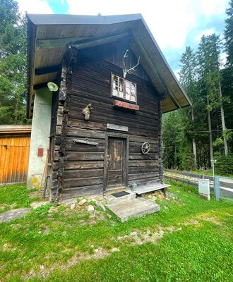Eine urige Alm mit traditioneller Holzfassade, umgeben von einer grünen Wiese und dichten Wäldern.