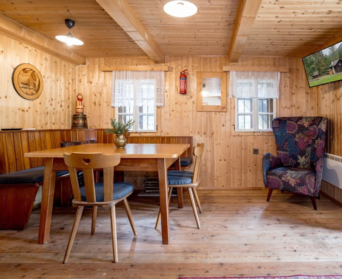 Ein gemütlicher Essbereich in der Alm mit einer rustikalen Holzsitzecke, warmem Licht und einem gemusterten Sessel.