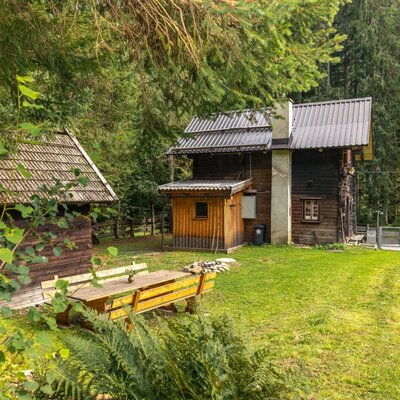 Die einladende Alm mit einem gepflegten, grünen Gartenbereich und einer rustikalen Holzsitzecke inmitten idyllischer Natur.