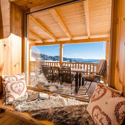 Blick aus dem Chalet mit Sitzbank auf die möblierte Terrasse und die winterliche Berglandschaft.