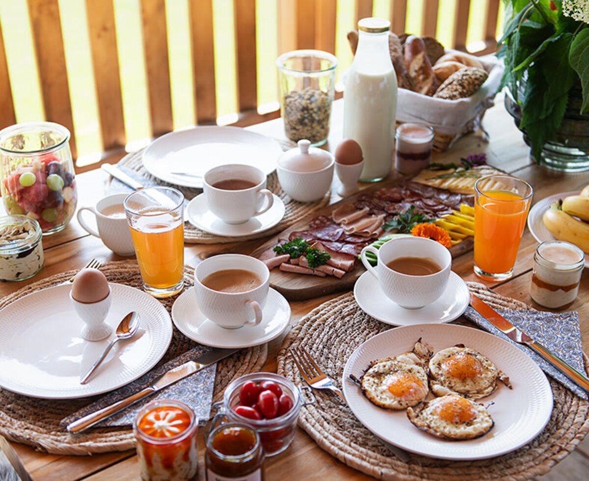 Reichhaltiges Frühstück auf der Terrasse des Chalets mit Spiegeleiern, Aufschnitt, Brot, Obst und Getränken.