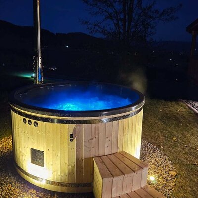 Hottub aus Holz mit blau beleuchtetem Wasser und Holzstufen im Freien des Chalets bei Nacht.