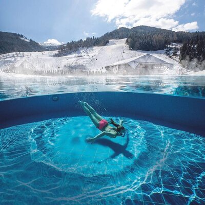 Poolbereich des Bauernhofs mit einem Gast, der schwimmt, und Blick auf schneebedeckte Berge und Skipisten.