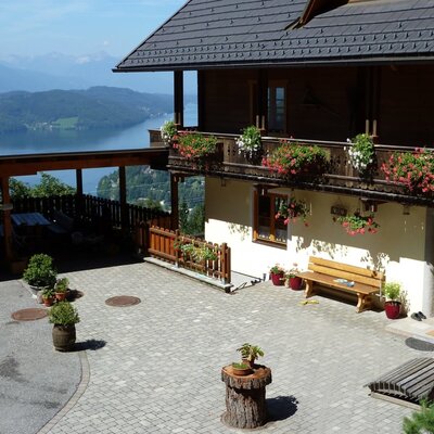 Außenansicht des Ferienhauses mit Balkonen, gepflastertem Hof, Carport und Seeblick sowie Bergblick.
