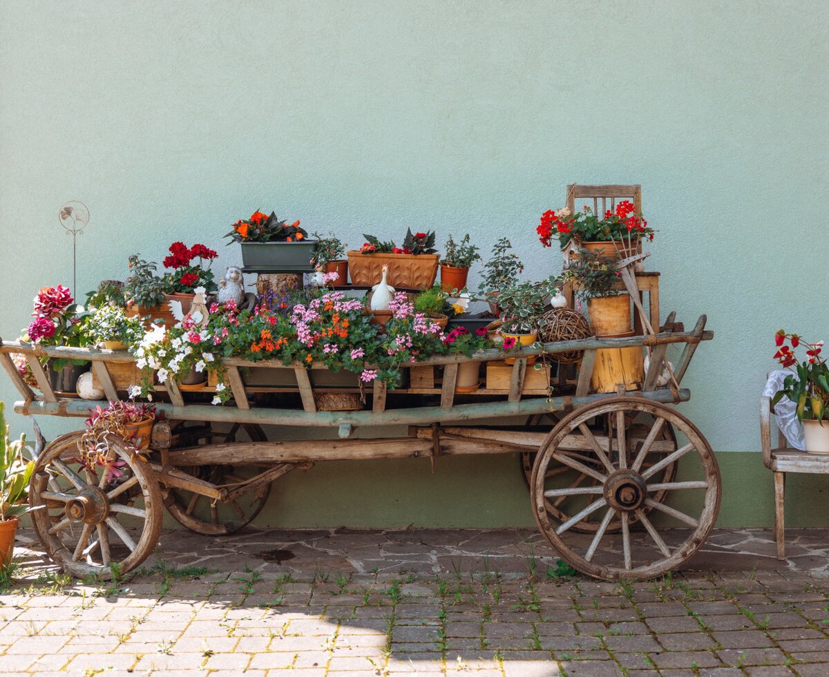 Ein liebevoll dekorierter Holzwagen mit bunten Blumen vor dem Bauernhof.
