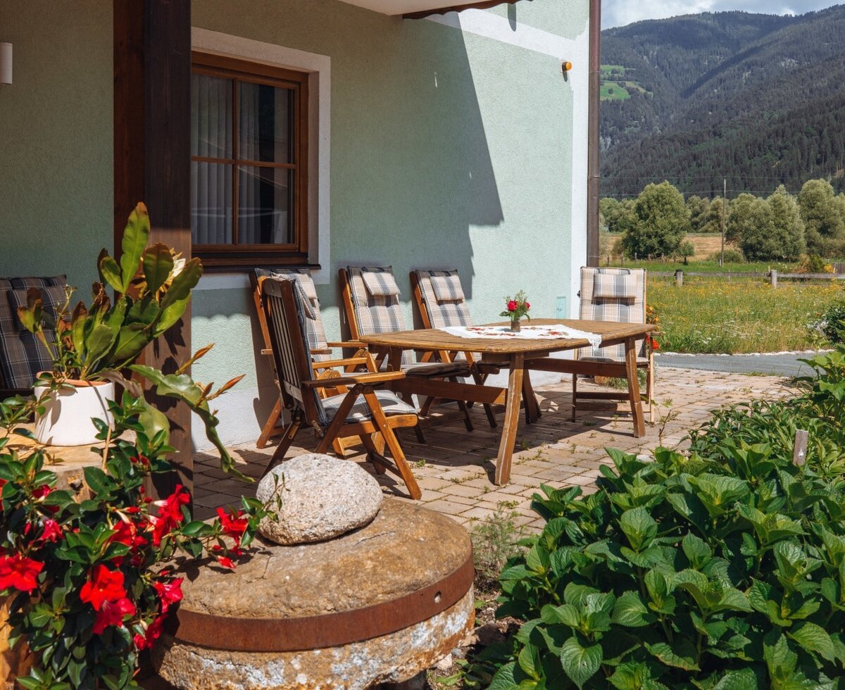 Die Terrasse des Bauernhofs mit einer Holzsitzgruppe und Bergblick.