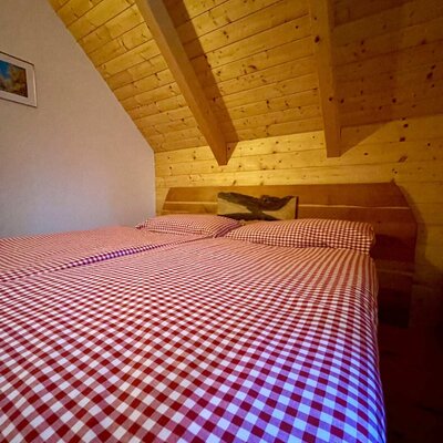Doppelbett mit rot-weiß karierter Bettwäsche in einem Schlafzimmer der Alm mit Holzdecken und Dachschrägen.