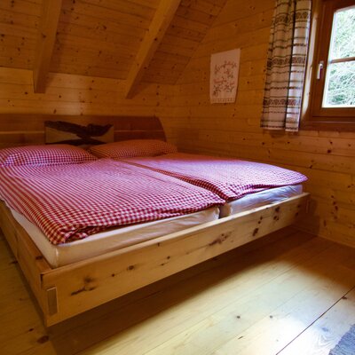Schlafzimmer in der Alm mit Holzbett, rot-weiß karierter Bettwäsche und Fenster.