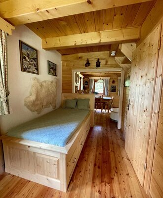 Ein gemütlicher Schlafbereich der Alm mit einem rustikalen Holzbett und warmen Holzelementen.